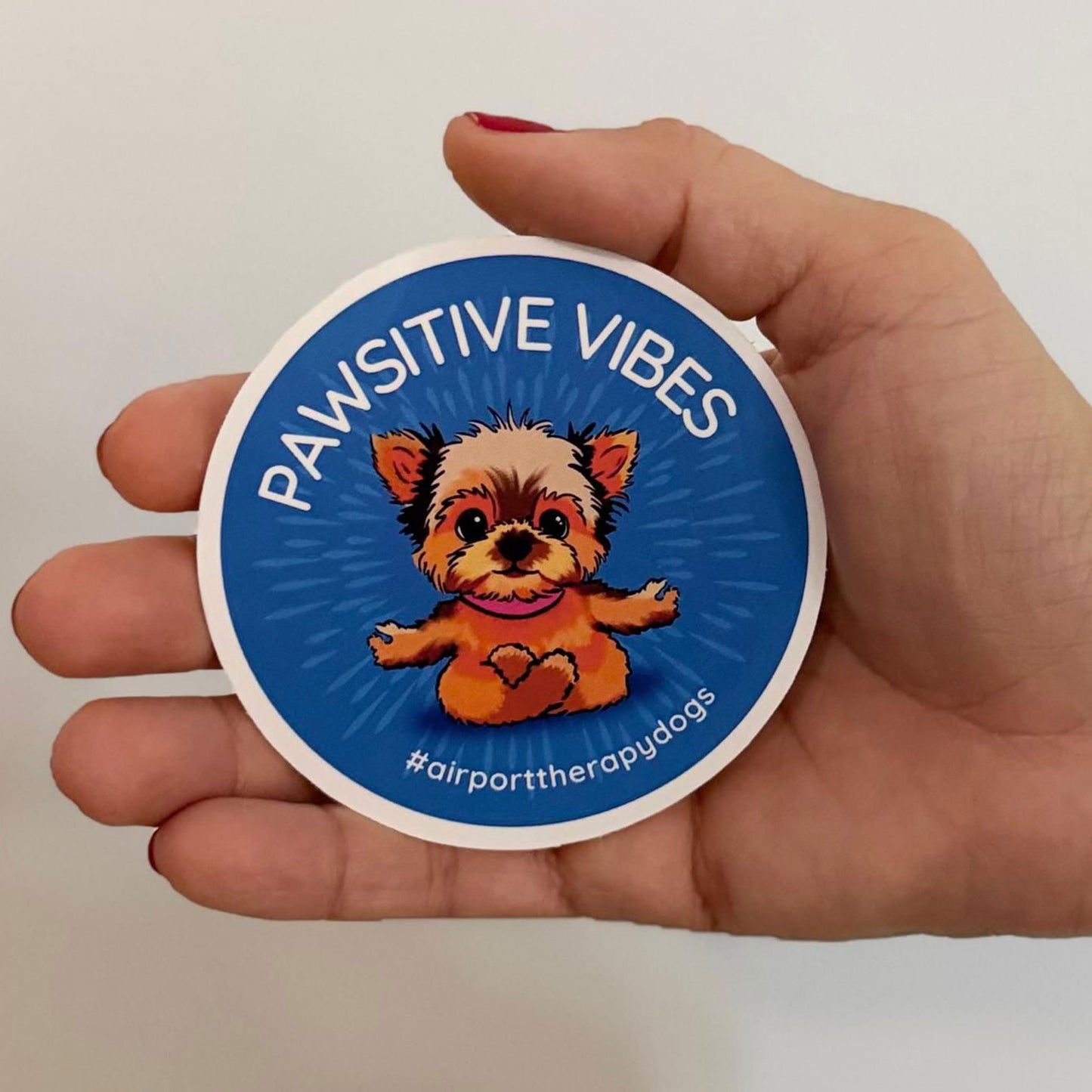 Hand holding a 3-inch wide "When Airports Suck" sticker to show scale, perfect size for water bottles and phone cases.