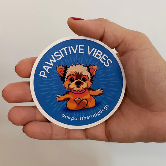 Hand holding a 3-inch wide "When Airports Suck" sticker to show scale, perfect size for water bottles and phone cases.